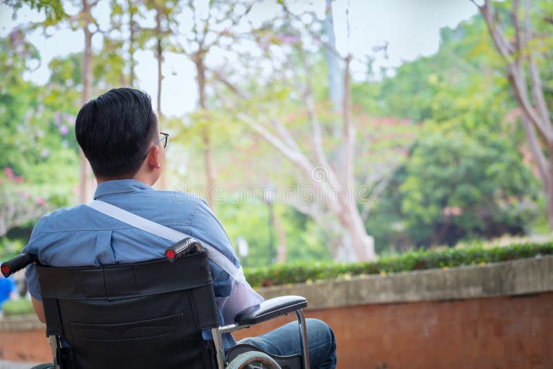 O homem deficiente na cadeira de rodas no parque, paciente dos jovens sozinhos é r imagem de stock royalty free O homem deficiente na cadeira de rodas no parque, paciente dos jovens sozinhos é r imagem de stock royalty free