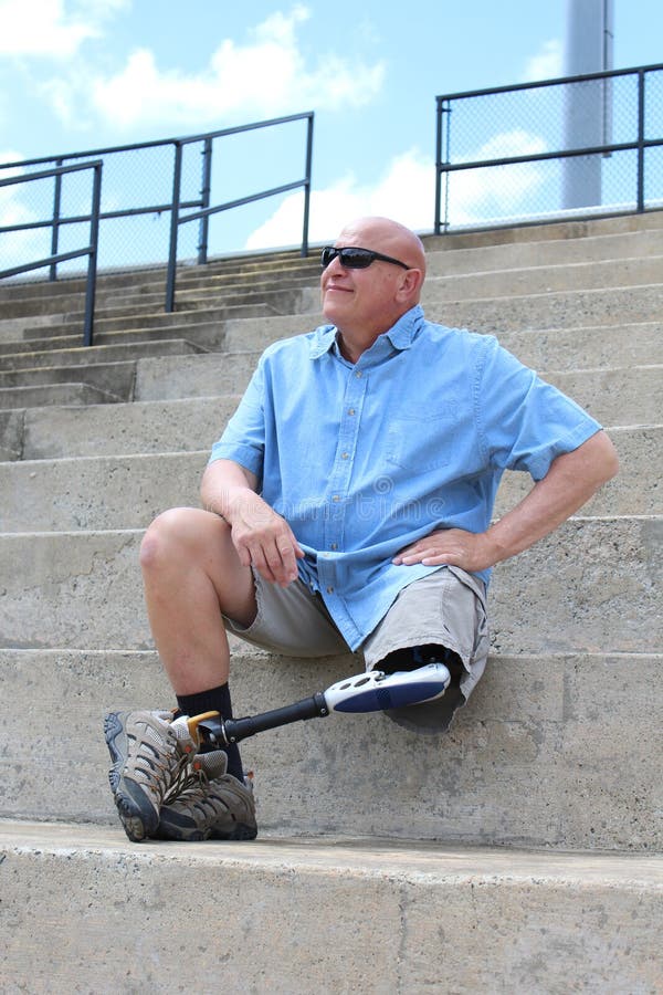 Man in blue shirt and grey shorts with a prosthetic leg, seated with hand on his hip. Man in blue shirt and grey shorts with a prosthetic leg, seated with hand on his hip