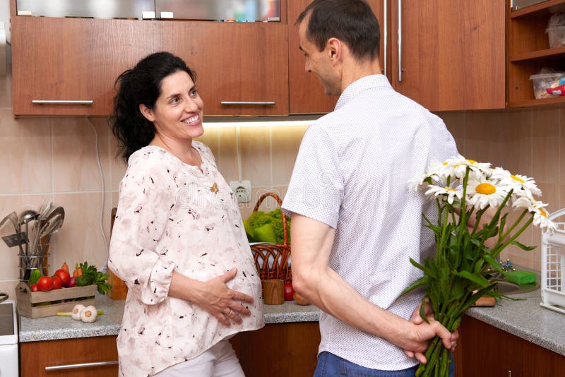 O homem dá flores da camomila à mulher gravida, par no interior com frutas e legumes frescas, conceito saudável da cozinha do ali imagens de stock royalty free O homem dá flores da camomila à mulher gravida, par no interior com frutas e legumes frescas, conceito saudável da cozinha do ali imagens de stock royalty free