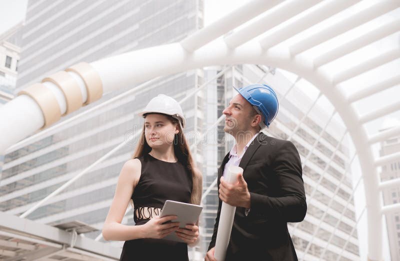 O homem e o coordenador industrial fêmea que mantêm uma tabuleta e os modelos que trabalham e que discutem no terreno de construç imagens de stock royalty free O homem e o coordenador industrial fêmea que mantêm uma tabuleta e os modelos que trabalham e que discutem no terreno de construç imagens de stock royalty free