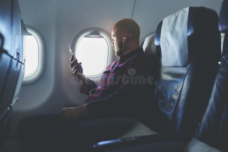 O homem está apreciando sua música favorita através do telefone de pilha, quando voar em um avião fotografia de stock O homem está apreciando sua música favorita através do telefone de pilha, quando voar em um avião fotografia de stock