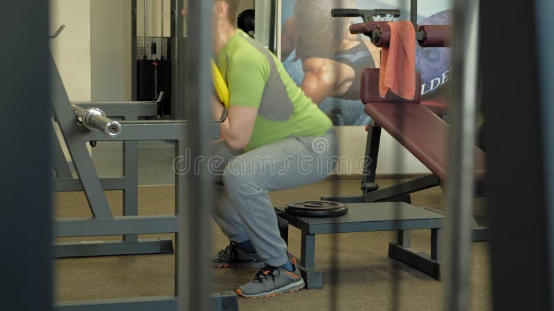 O homem excesso de peso faz ocupas com ocupas com um disco do peso para um barbell Homem da aptid?o training Conceito saud?vel do filme O homem excesso de peso faz ocupas com ocupas com um disco do peso para um barbell Homem da aptid?o training Conceito saud?vel do filme