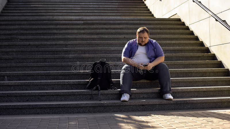 O homem gordo que escuta a música em escadas, solidão, excesso de peso causa inseguranças imagem de stock O homem gordo que escuta a música em escadas, solidão, excesso de peso causa inseguranças imagem de stock