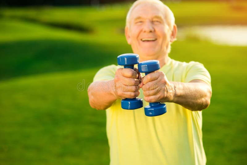 O homem idoso está guardando pesos imagem de stock royalty free O homem idoso está guardando pesos imagem de stock royalty free