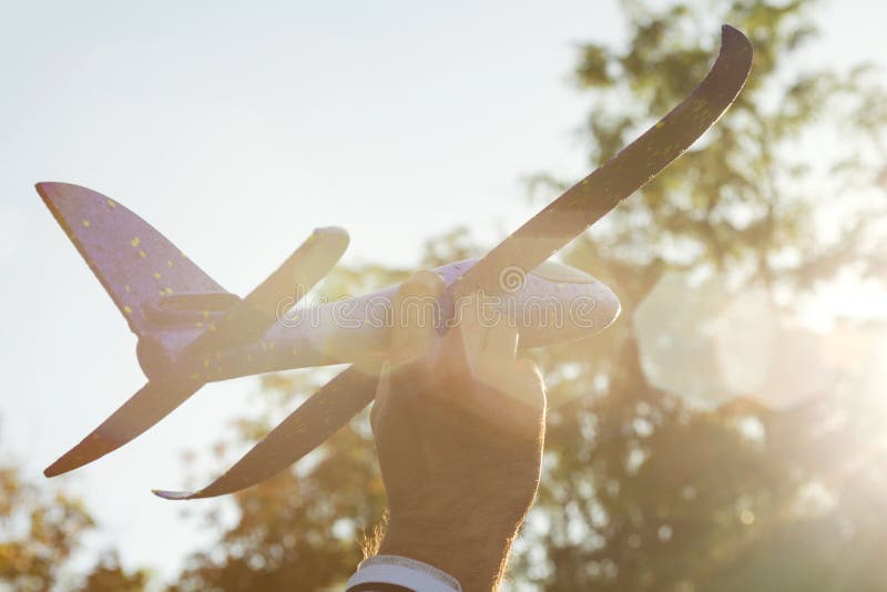 O homem joga com um avião do brinquedo no por do sol e nos sonhos da viagem Mão com fim pequeno do plano acima Avião do brinquedo fotografia de stock O homem joga com um avião do brinquedo no por do sol e nos sonhos da viagem Mão com fim pequeno do plano acima Avião do brinquedo fotografia de stock