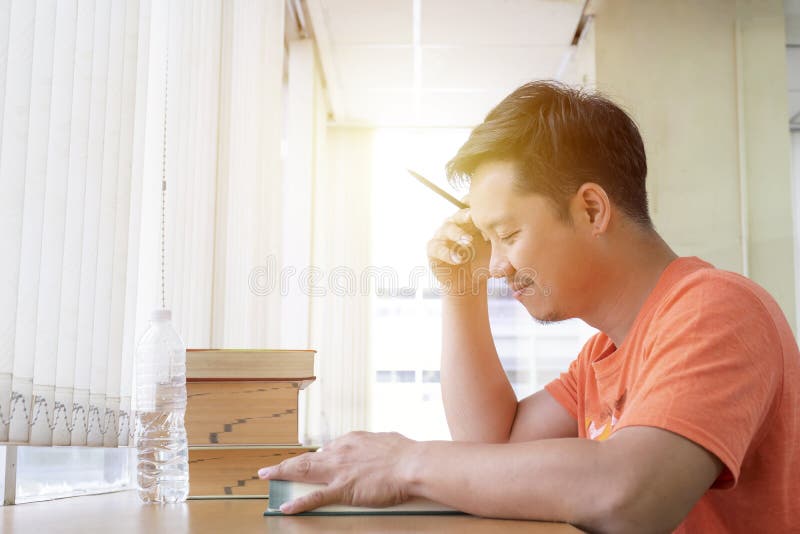 O homem novo concentrado está lendo um livro, sentando-se na tabela e no wr fotografia de stock royalty free O homem novo concentrado está lendo um livro, sentando-se na tabela e no wr fotografia de stock royalty free