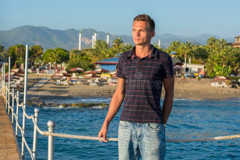 O homem novo considerável nos óculos de sol está em um cais no backgro foto de stock O homem novo considerável nos óculos de sol está em um cais no backgro foto de stock