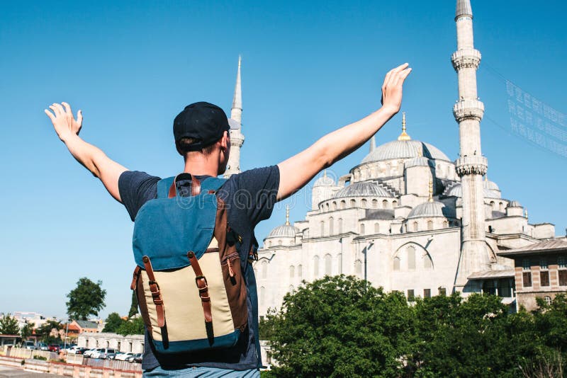 O homem novo do turista ao lado da mesquita azul mundialmente famosa em Istambul levantou suas mãos que mostram como feliz e livr imagem de stock O homem novo do turista ao lado da mesquita azul mundialmente famosa em Istambul levantou suas mãos que mostram como feliz e livr imagem de stock