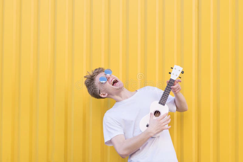 O homem novo louco joga a uquelele em um fundo amarelo Músico expressivo que joga a guitarra Conceito musical foto de stock O homem novo louco joga a uquelele em um fundo amarelo Músico expressivo que joga a guitarra Conceito musical foto de stock