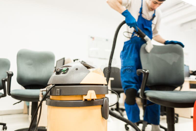 O homem novo no workwear e nas luvas de borracha limpa a cadeira do escrit?rio com o equipamento profissional foto de stock royalty free O homem novo no workwear e nas luvas de borracha limpa a cadeira do escrit?rio com o equipamento profissional foto de stock royalty free