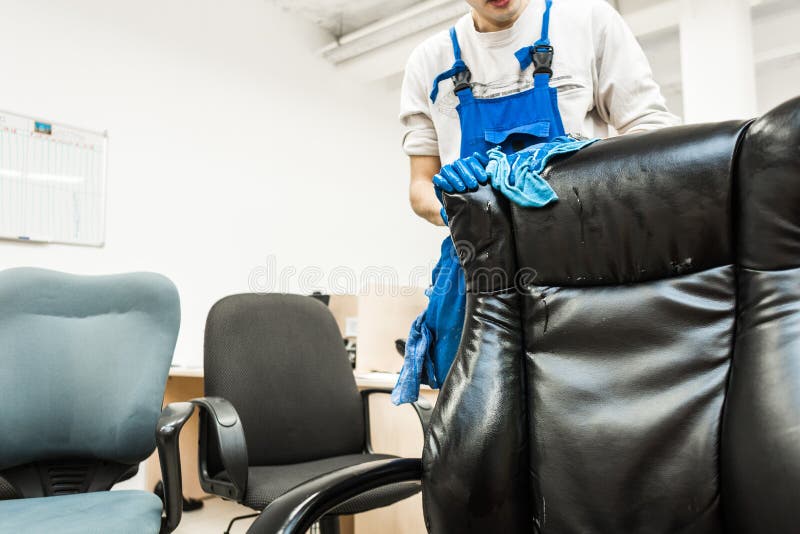 O homem novo no workwear e nas luvas de borracha limpa a cadeira do escrit?rio com o equipamento profissional imagem de stock royalty free O homem novo no workwear e nas luvas de borracha limpa a cadeira do escrit?rio com o equipamento profissional imagem de stock royalty free