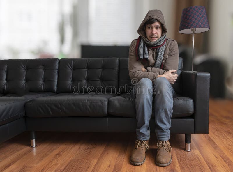 O homem novo que senta-se no sofá está sentindo frio em casa