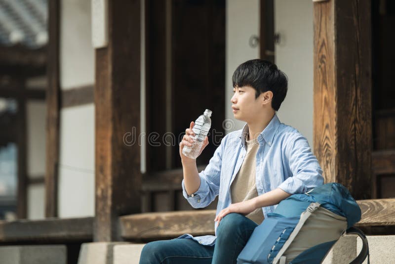 O homem novo que viaja a Coreia está tomando um resto com uma garrafa de água imagens de stock royalty free O homem novo que viaja a Coreia está tomando um resto com uma garrafa de água imagens de stock royalty free
