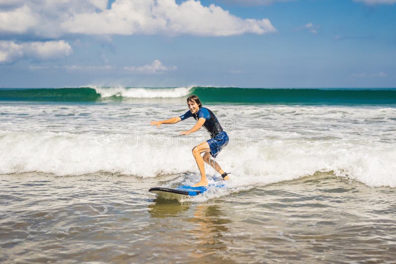 O homem novo, surfista do novato aprende surfar em uma espuma do mar no B foto de stock royalty free O homem novo, surfista do novato aprende surfar em uma espuma do mar no B foto de stock royalty free