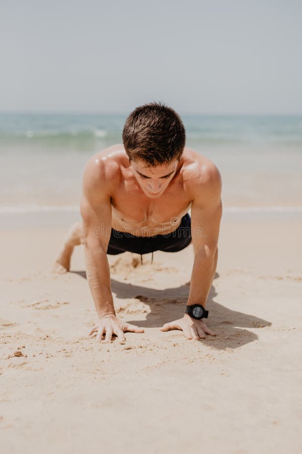O homem que da aptidão exercitar empurra levanta o sorriso feliz Cruz-treinamento masculino do modelo da aptidão na praia