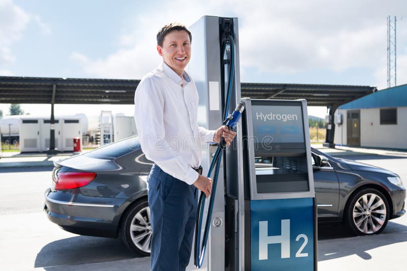 O homem segura um bocal a hidrogênio numa estação de reabastecimento de hidrogênio. Carro de reabastecimento com combustível de hi fotos de stock