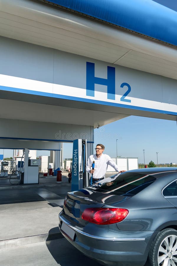 O homem segura um bocal a hidrogênio numa estação de reabastecimento de hidrogênio. Carro de reabastecimento com combustível de hi imagem de stock