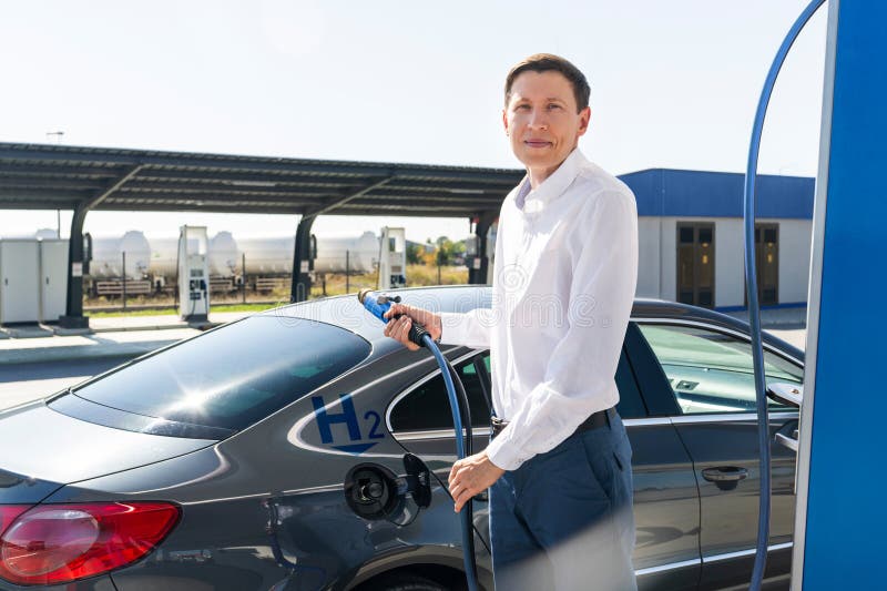 O homem segura um bocal a hidrogênio numa estação de reabastecimento de hidrogênio. Carro de reabastecimento com combustível de hi imagens de stock royalty free