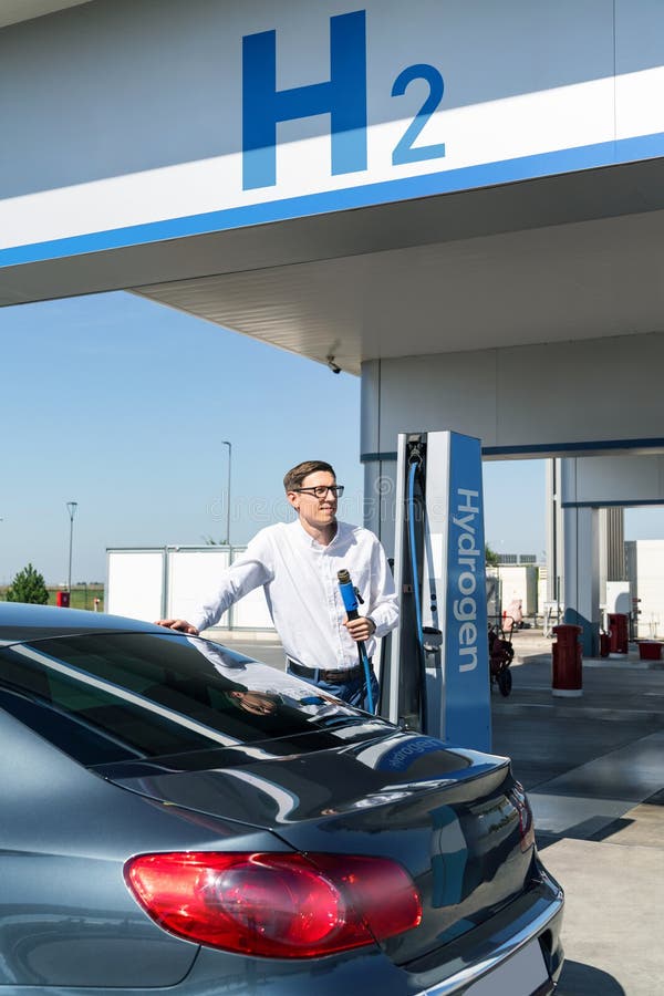 O homem segura um bocal a hidrogênio numa estação de reabastecimento de hidrogênio. Carro de reabastecimento com combustível de hi fotos de stock