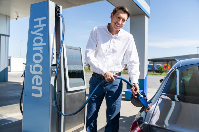 O homem segura um bocal a hidrogênio numa estação de reabastecimento de hidrogênio. Carro de reabastecimento com combustível de hi imagens de stock royalty free