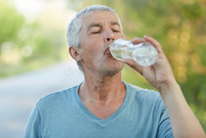 O homem superior sedento bebe a água da garrafa palstic, sendo cansado após o cardio- treinamento, tem o estilo de vida ativo, ve foto de stock O homem superior sedento bebe a água da garrafa palstic, sendo cansado após o cardio- treinamento, tem o estilo de vida ativo, ve foto de stock