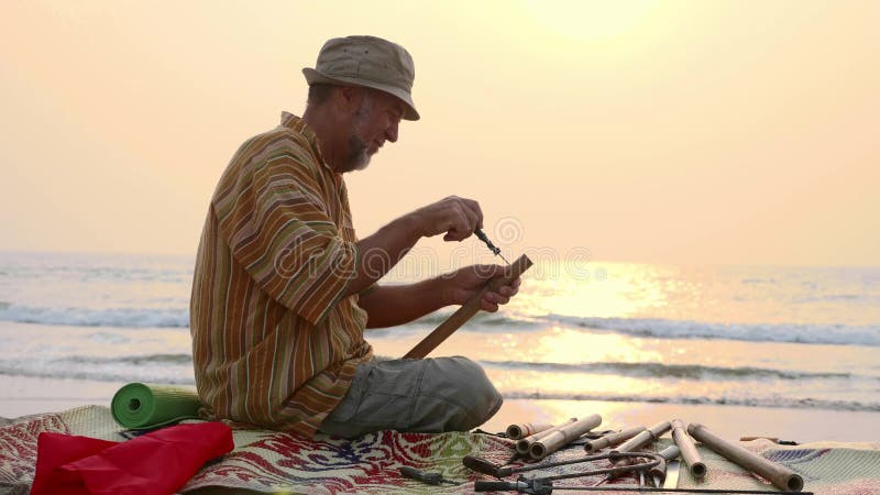 O homem superior senta-se na praia e flauta da fatura pelas mãos