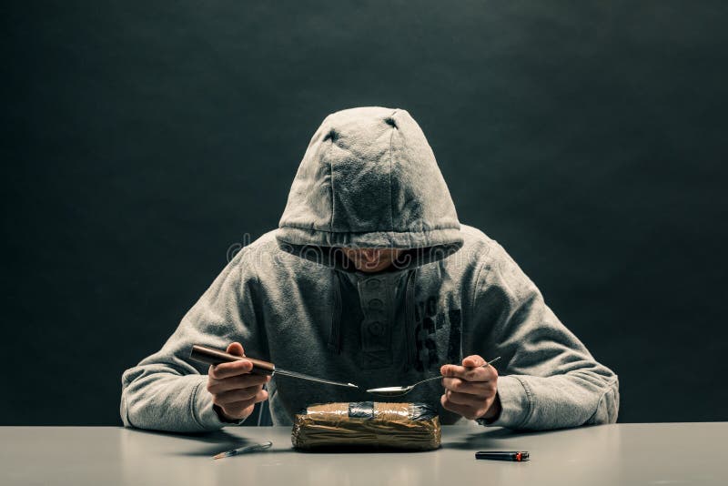 O homem é um viciado em drogas sentado à mesa faz drogas O conceito de problemas sociais da toxicodependência e da criminalidade fotografia de stock O homem é um viciado em drogas sentado à mesa faz drogas O conceito de problemas sociais da toxicodependência e da criminalidade fotografia de stock