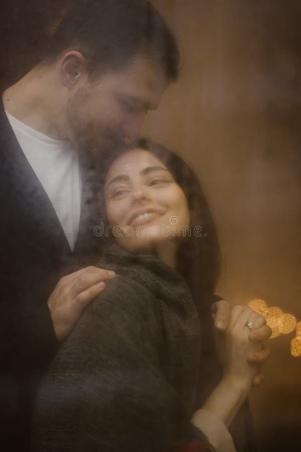 O indivíduo de amor abraça e beija sua posição feliz da amiga atrás de uma janela molhada com luzes Pares rom?nticos foto de stock O indivíduo de amor abraça e beija sua posição feliz da amiga atrás de uma janela molhada com luzes Pares rom?nticos foto de stock