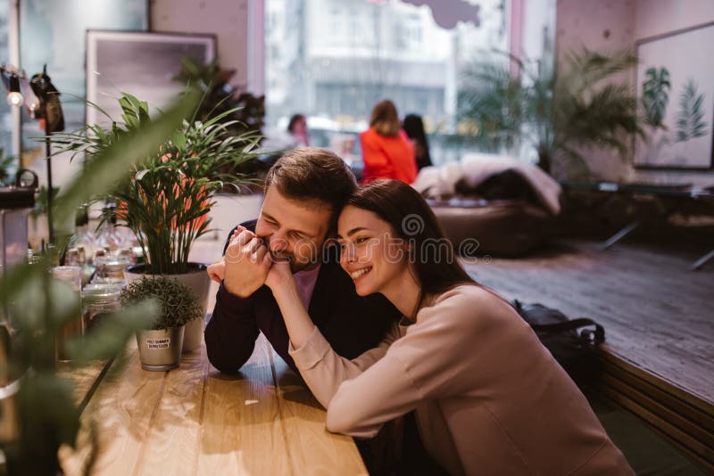 O indivíduo de amor feliz guarda e morde a mão da sua amiga que senta-se na tabela no café e olha-a imagens de stock O indivíduo de amor feliz guarda e morde a mão da sua amiga que senta-se na tabela no café e olha-a imagens de stock