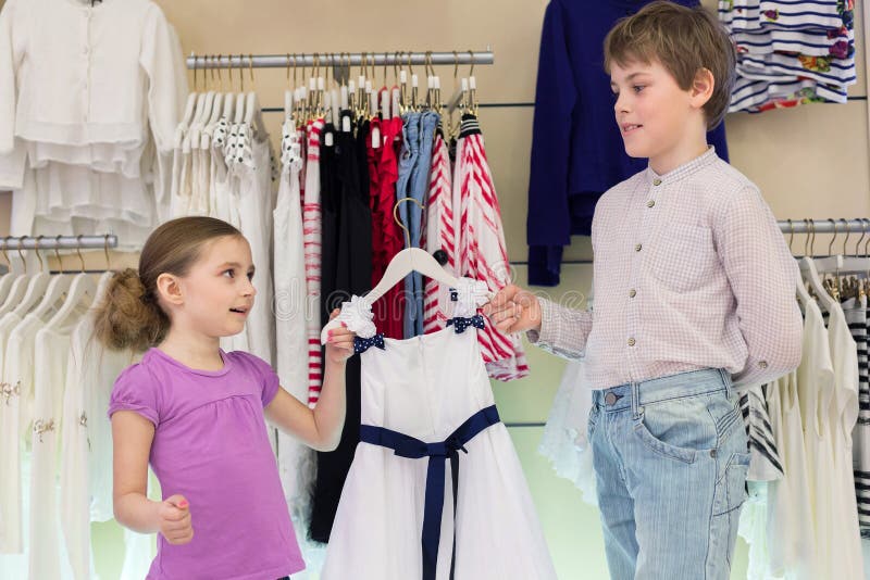 The brother helps sister to choose clothes in shop of childrens clothing. The brother helps sister to choose clothes in shop of childrens clothing