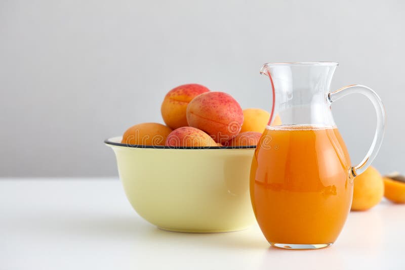 O jarro de vidro com suco fresco e os abricós maduros rolam foto de stock O jarro de vidro com suco fresco e os abricós maduros rolam foto de stock