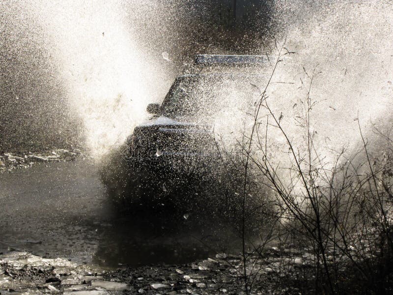 Four-wheel-drive vehicle plows through mountain stream creating large spray of water. Four-wheel-drive vehicle plows through mountain stream creating large spray of water