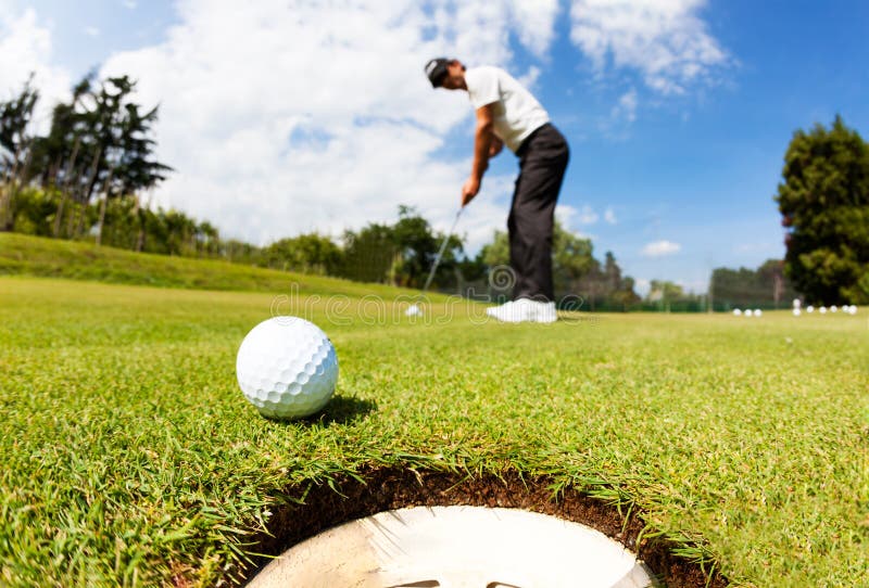O jogador de golfe conduziu a bola no furo no verde de colocação; sol do verão fotos de stock O jogador de golfe conduziu a bola no furo no verde de colocação; sol do verão fotos de stock