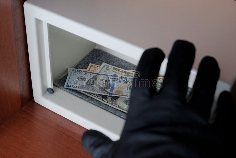 O ladrão rouba notas de dólar de um cofre forte com um fechamento de combinação Proteção incerta Uma mão preto-gloved alcança par imagem de stock O ladrão rouba notas de dólar de um cofre forte com um fechamento de combinação Proteção incerta Uma mão preto-gloved alcança par imagem de stock