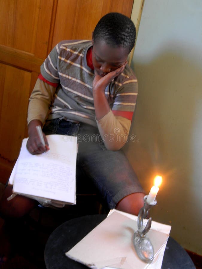 O livro de leitura pensativo do menino na vela iluminou a sala imagens de stock O livro de leitura pensativo do menino na vela iluminou a sala imagens de stock