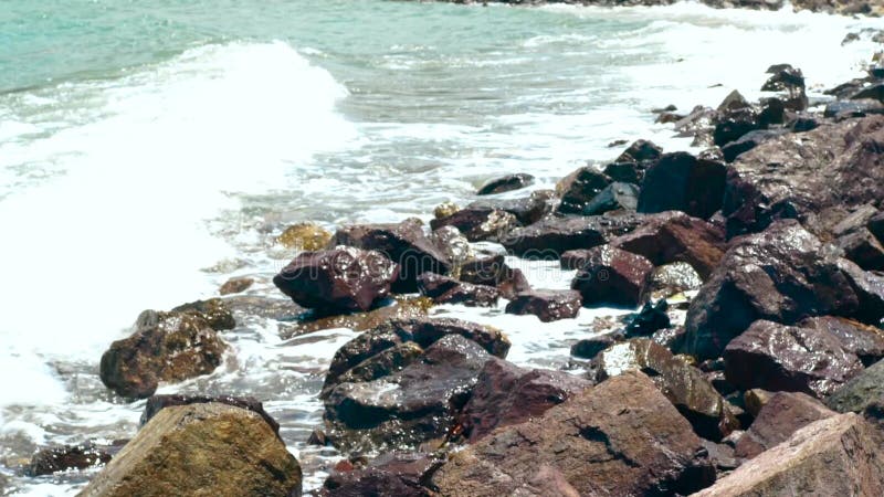 O mar acena a água na praia rochosa no dia de verão Feche acima das ondas de água que espirram na praia do oceano O mar bonito ac