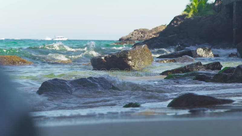 O mar acena a água que espirra na praia rochosa na ilha tropical As ondas de água que espirram no oceano costeiam o mar bonito