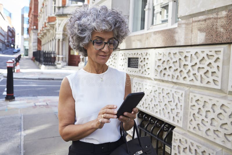 O meio envelheceu a mulher que usa o smartphone na rua da cidade fotos de stock O meio envelheceu a mulher que usa o smartphone na rua da cidade fotos de stock