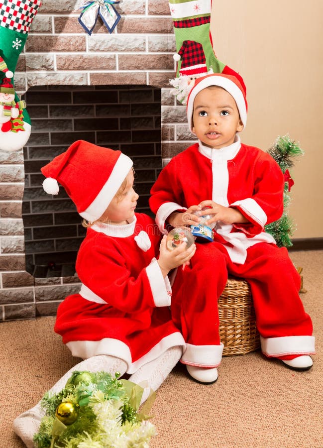 O menino afro-americano e a menina vestiram o traje Santa Claus pela chaminé Natal imagens de stock O menino afro-americano e a menina vestiram o traje Santa Claus pela chaminé Natal imagens de stock