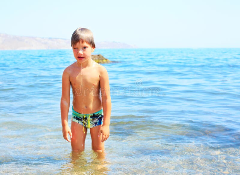 O menino alegre do llittle aprecia o jogo com água na praia imagem de stock O menino alegre do llittle aprecia o jogo com água na praia imagem de stock