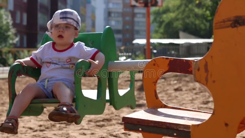 O menino considerável pequeno nos vidros monta no carrossel