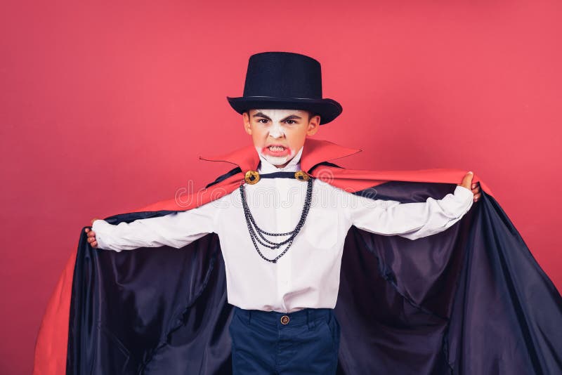 Menino vampiro de halloween acena sua capa preta e vermelha com as mãos  rodeadas sobre o fundo vermelho do estúdio. maquiagem de vampiro de  criança.