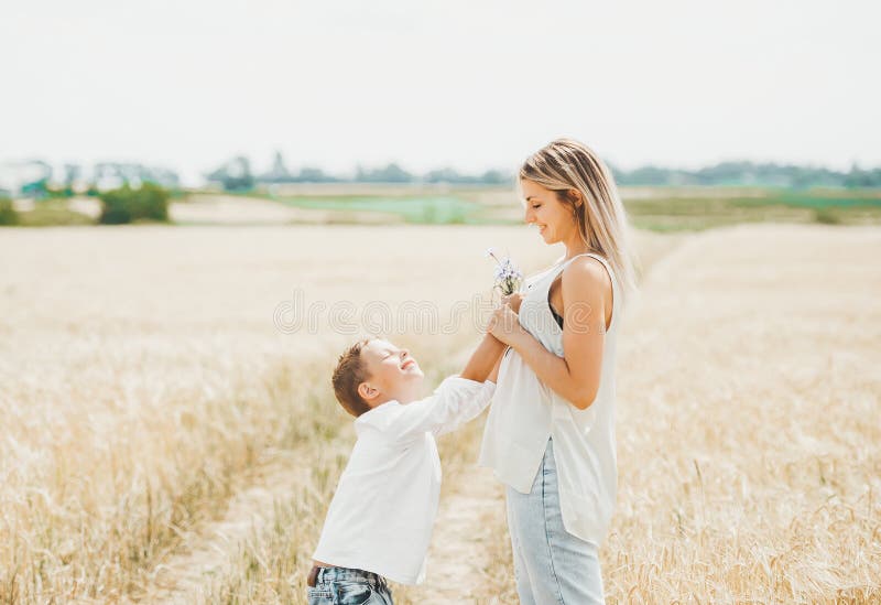 O menino dá a sua mãe um ramalhete dos wildflowers no campo de trigo ensolarado foto de stock O menino dá a sua mãe um ramalhete dos wildflowers no campo de trigo ensolarado foto de stock