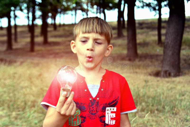 O menino guarda uma ampola incandescente, que se queime em sua mão e se olhe a com surpresa e admiração foto de stock royalty free O menino guarda uma ampola incandescente, que se queime em sua mão e se olhe a com surpresa e admiração foto de stock royalty free