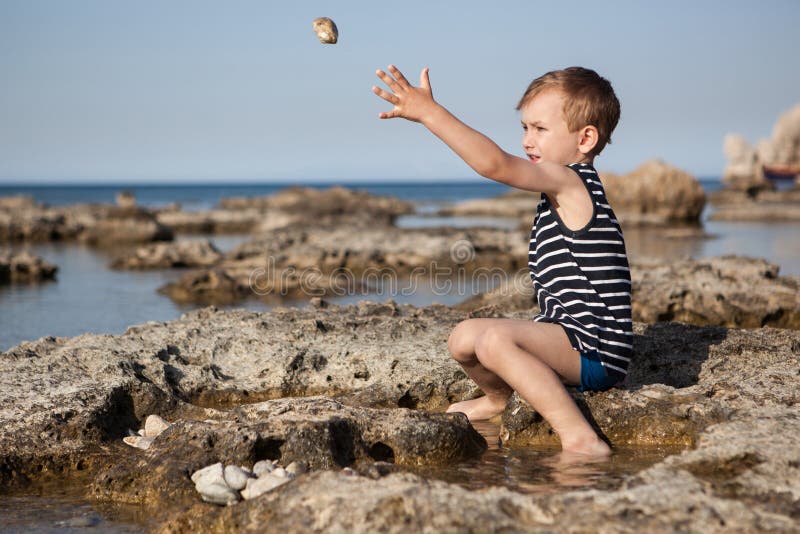 O menino joga pedras no mar imagens de stock O menino joga pedras no mar imagens de stock