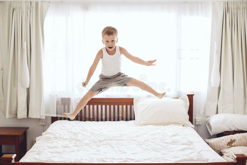 O menino que salta na cama foto de stock O menino que salta na cama foto de stock