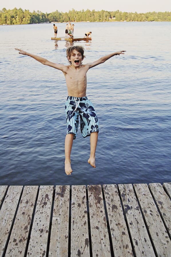 O menino que salta no lago foto de stock O menino que salta no lago foto de stock