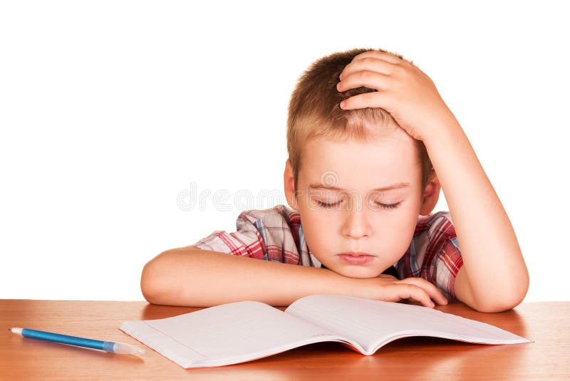 O menino que senta-se na tabela caiu adormecido no livro de exercício isolado imagem de stock royalty free O menino que senta-se na tabela caiu adormecido no livro de exercício isolado imagem de stock royalty free