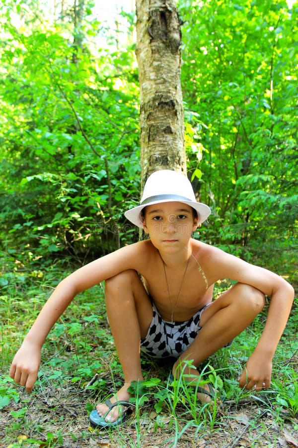 O menino senta-se na grama perto do vidoeiro fotografia de stock O menino senta-se na grama perto do vidoeiro fotografia de stock