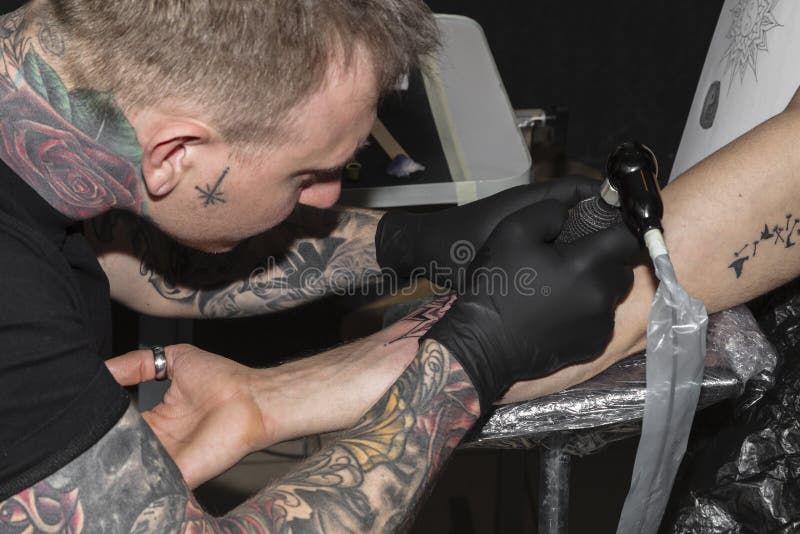 O mestre da tatuagem faz a tatuagem preta na mão masculina imagem de stock O mestre da tatuagem faz a tatuagem preta na mão masculina imagem de stock